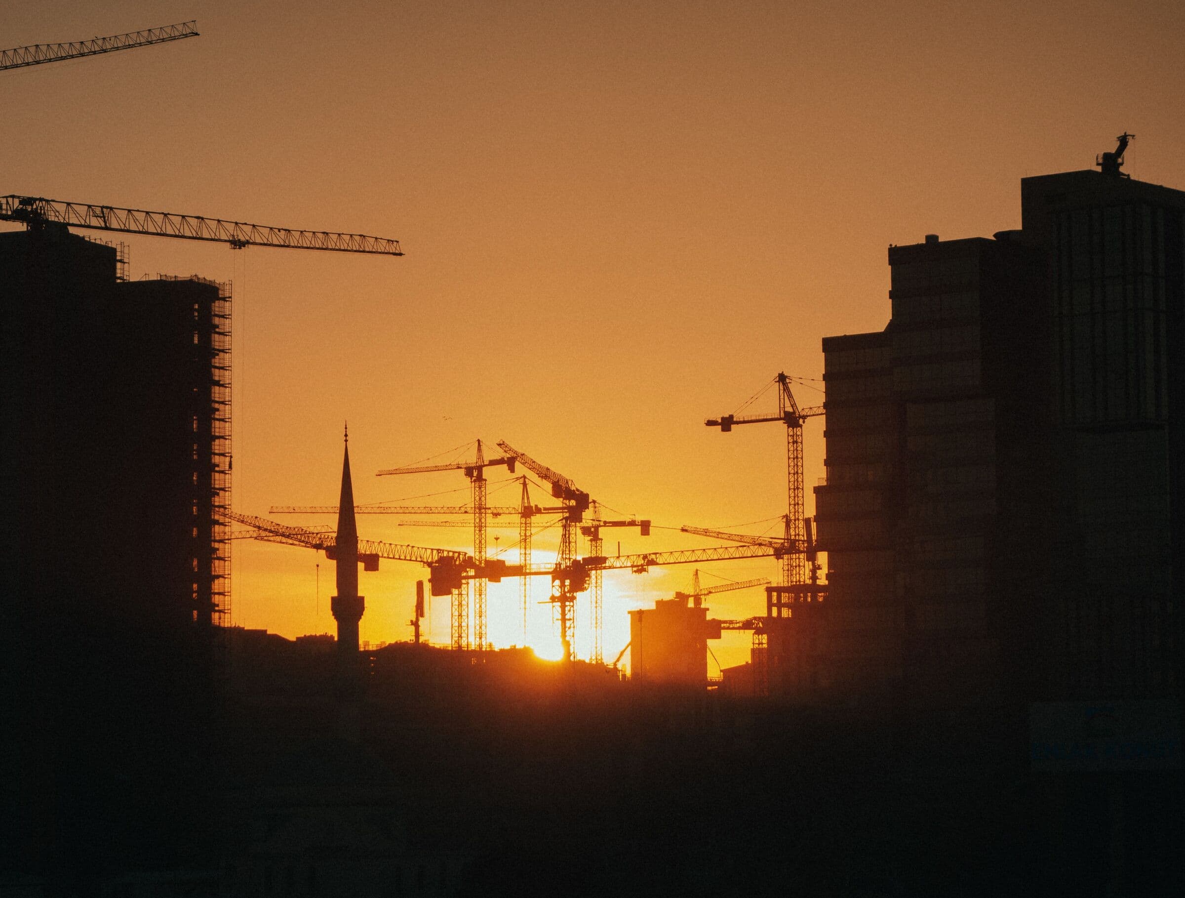 Towers under construction and tower cranes silhouetted against the setting sun